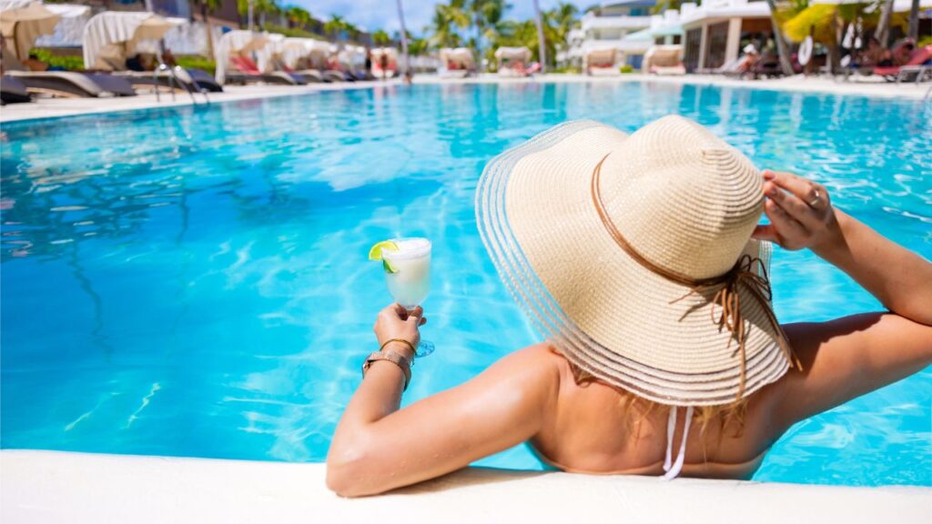 A woman with a hat in a pool holding a margarita.